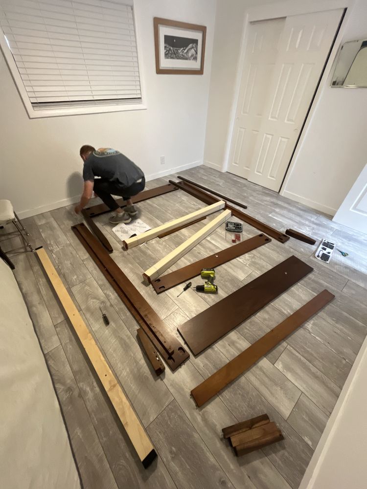 A Joe's worker assembling a wooden bed frame in a bedroom.
