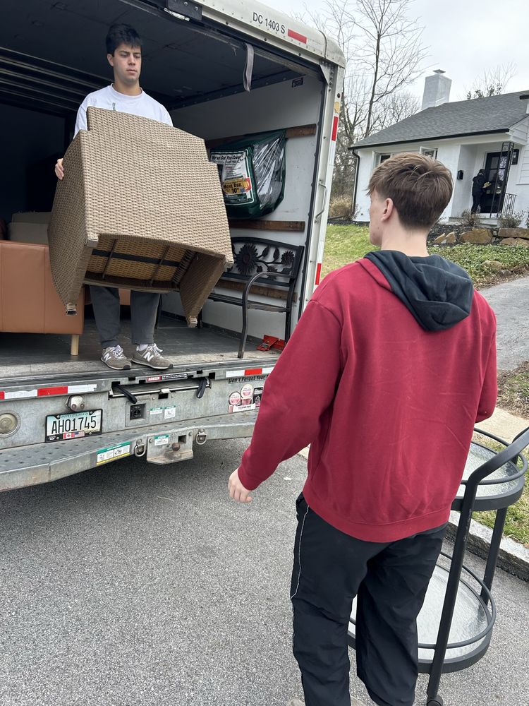 Joe's worker carrying a load out of a moving truck while a teammate waits to help.